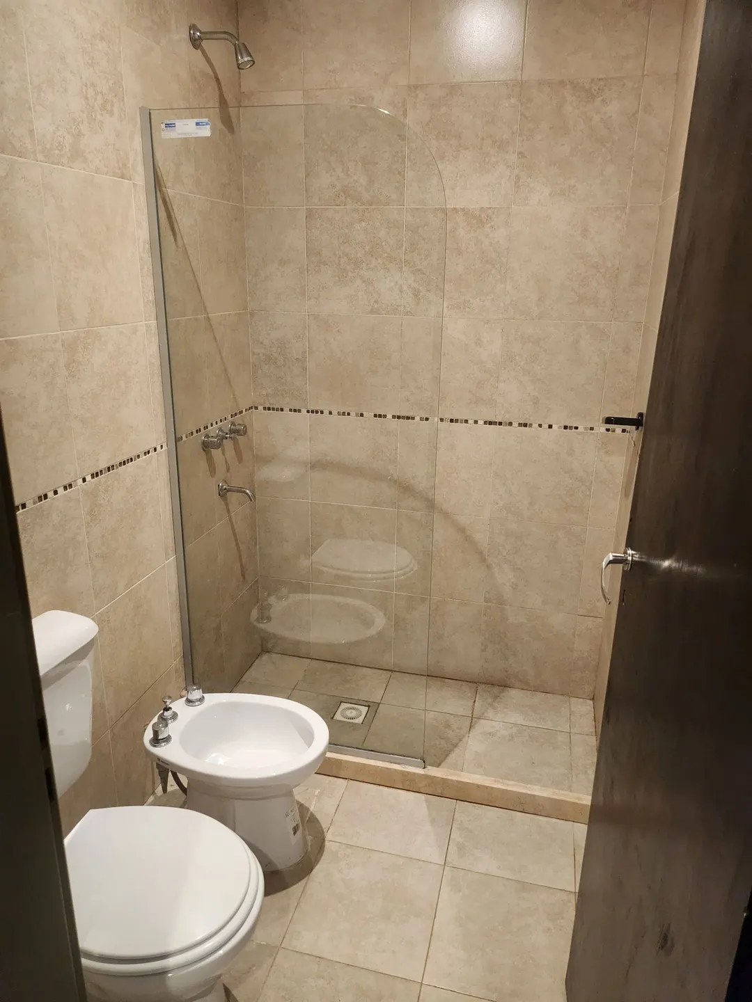 Baño con ducha y mampara de vidrio, inodoro y bidé, revestido en tonos claros