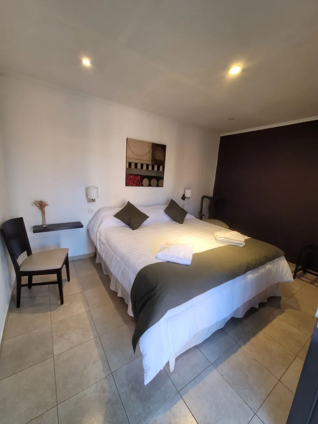 Cama matrimonial con almohadones verdes y toallas sobre la ropa de cama blanca
