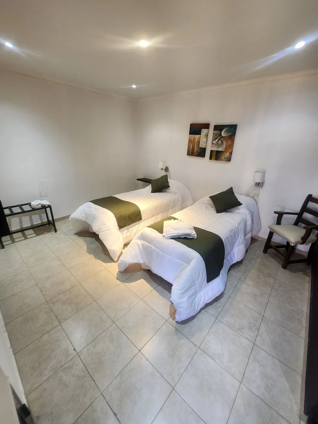 Habitación luminosa con dos camas individuales, almohadones verdes y cuadros
