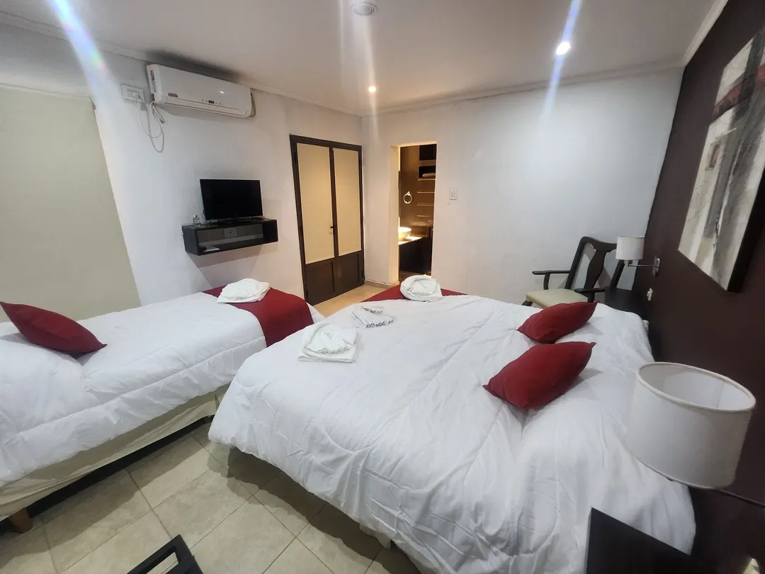 Cama matrimonial y cama individual con almohadones rojos, TV y aire acondicionado