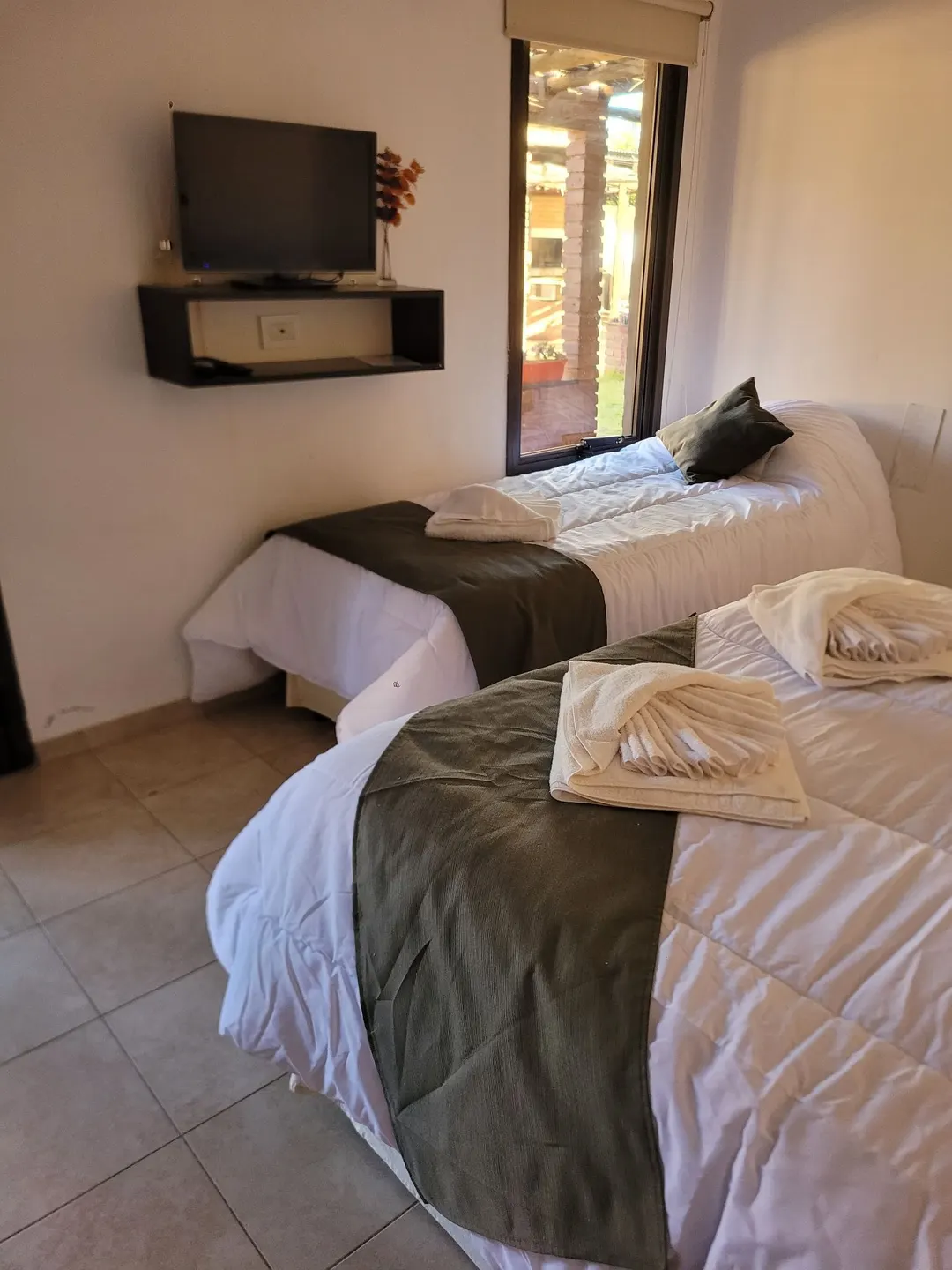 Toallas dobladas sobre las camas, con televisor y ventana hacia la galería del patio